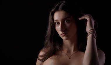 Uzun kahverengi saçlı, bilezik ve kolye takan, yoğun görünüşlü genç bir kadının stüdyo portresi