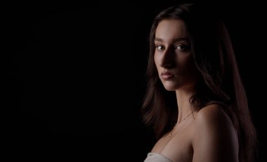 Stüdyoda siyah arka planda poz veren uzun kahverengi saçlı güzel bir genç kadın.