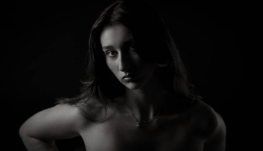 Uzun kahverengi saçlı, siyah arka planda poz veren güzel bir kadının stüdyo portresi.