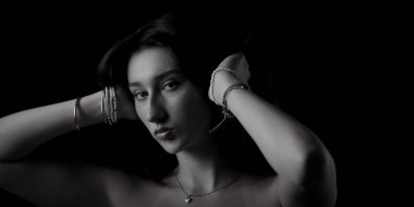 Güzel bir genç kadının siyah beyaz portresi. Bilezik ve kolye takıyor, saçlarını tutuyor.