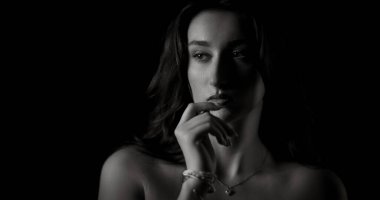 Düşünceli bir ifadeyle poz veren, eliyle çenesine dokunan güzel bir genç kadının stüdyo portresi.