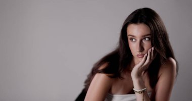 Uzun kahverengi saçlı genç bir kadının stüdyo portresi. Yüzünü kameraya çevirmeden yüzünü dinlendiriyordu.