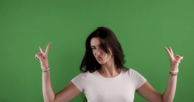 Genç bir kadın komik bir yüz ifadesi takınıyor ve iki eli de krom anahtarlı barış işareti gösteriyor.