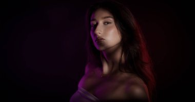 Yüzüne ve vücuduna mor ışıklar yansıtılmış genç bir kadının stüdyo portresi.