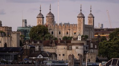 Londra Kulesi 'nin günbatımında bayrağını indirirken tarihi taş duvarları ve kuleleri Londra, İngiltere' de bulutlu bir gökyüzüne karşı gösteriyor.