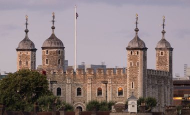 Londra Kulesi 'nin günbatımında bayrağını indirirken tarihi taş duvarları ve kuleleri Londra, İngiltere' de bulutlu bir gökyüzüne karşı gösteriyor.