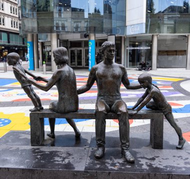 CARDIFF, İngiltere - 8 Ağustos 2025 - Cardiff şehir merkezinde, Galler 'de bir bankta oturan bir ailenin bronz heykeli