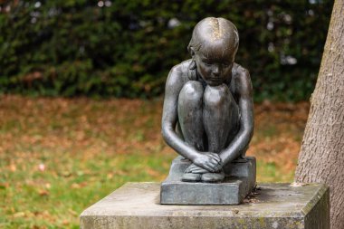 CARDIFF, İngiltere - 8 AĞUSTOS 2025 - Galler 'in Cardiff kentinde bir parkta ellerini ayaklarına dolamış düşünceli bir kızın bronz heykeli