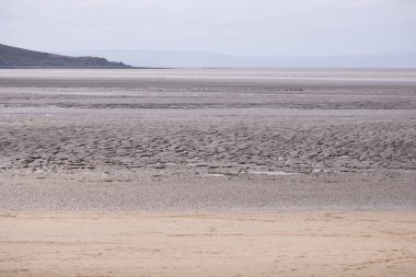 Weston Super Mare 'de bulutlu bir gökyüzünün altında alçak gelgit ve uzak tepeler ve deniz ile çatlak çamur düzlüklerinin manzarası
