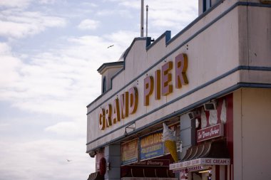 WESTON, UK - 8 AĞUSTOS 2025 - Birleşik Krallık 'ta Weston Super Mare' de uçan martılarla bulutlu gökyüzünün altındaki Grand Pier tabelası