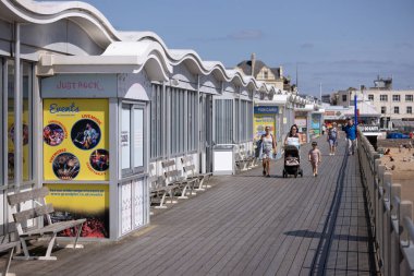 WESTON, UK - 8 AĞUSTOS 2025 - Aileler güneşli bir yaz gününün tadını çıkarıyorlar Weston Super Mare Grand Pier 'ın sahil ve eğlence mekanlarıyla sahil yolunda yürüyorlar.