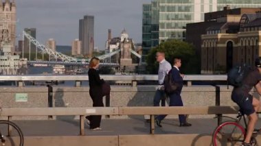 LONDON, İngiltere - 5 AĞUSTOS 2025 - İş adamları ve bisikletçiler gün batımında Londra köprüsünde kule köprüsü ve arka planda HMS Belfast ile seyahat ediyorlar