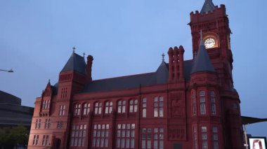 CARDIFF, İngiltere - 8 AĞUSTOS 2025 - Cardiff Bay 'deki Pierhead Binası güneş batarken kıpkırmızı parlıyor, kendine özgü saat kulesini ve karmaşık mimarisini gözler önüne seriyor