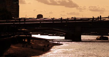 LONDON, İngiltere - 5 AĞUSTOS 2025 Blackfriars Köprüsü 'nde yürüyen ve Londra Thames Nehri üzerinde günbatımının tadını çıkaran turist siluetleri
