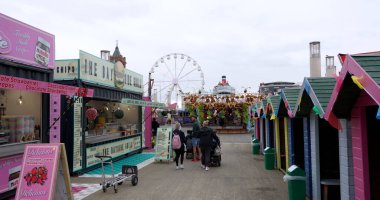 CARDIFF, İngiltere - 8 AĞUSTOS 2025 - Cardiff Körfezi 'ndeki turistler, dönme dolap ve renkli sahil kulübeleriyle eğleniyorlar.