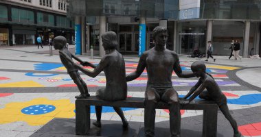 CARDIFF, İngiltere - 8 Ağustos 2025 - Cardiff, Galler 'de bir bankta oturan bir ailenin bronz heykeli, birlik ve aşkı temsil ediyor.