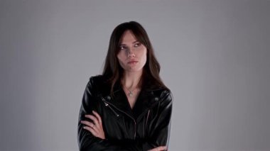 Siyah deri ceket giyen, kollarını kavuşturmuş sinirli ve şüpheci görünen genç bir kadının stüdyo portresi.