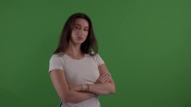 Kollarını kavuşturmuş genç bir kadın yeşil ekranda ciddi görünüyor.