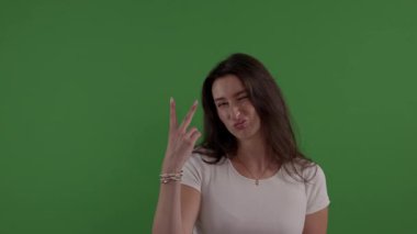 Genç bir kadın parmaklarıyla barış işareti gösteriyor ve krom anahtar arka planında göz kırpıyor.