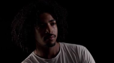 Siyah arka plana bakan kıvırcık saçlı, düşünceli, Afro-Amerikan bir adamın portresi.