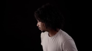 Siyah arka planda kameradan bakan kıvırcık saçlı bir yetişkinin portresi.