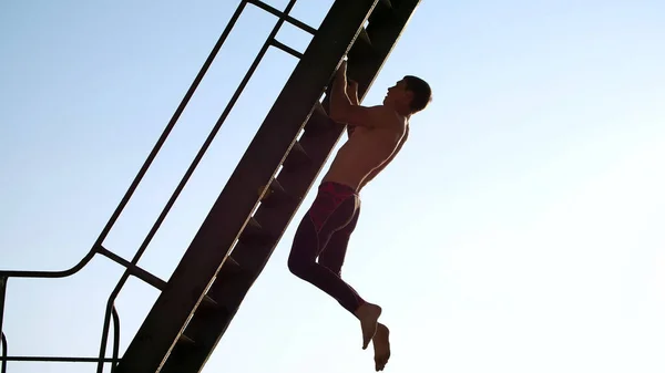 一个赤身裸体的年轻运动员 进行力量训练 挂在金属楼梯上 在一个货运港口 在日出时分 在夏天 高质量的照片 — 图库照片