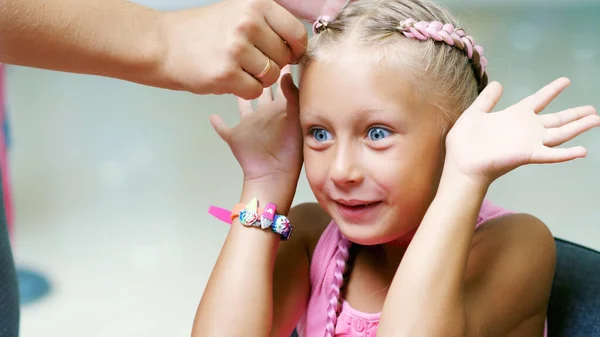 stock image Beautiful blond girl, of seven years old, braided two pigtails, do a hairstyle with pink locks of hair in a beauty salon, a hairdressers salon, in front of a large mirror. a little princess. High