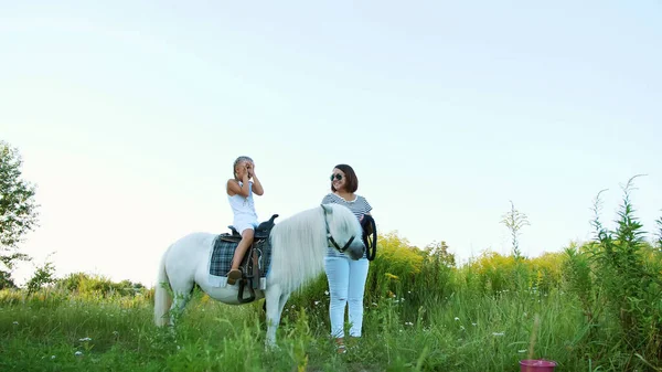 母親と娘のフィールドの周りを歩いている 娘はポニーに乗っている 母親はブライドルのためのポニーを保持している 陽気で幸せな家族の休暇 屋外では 夏には 森の近く 高品質 — ストック写真