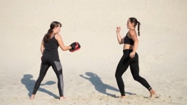 Siyah fitness uygun bir çift nişanlandık iki atletik, genç kadınlarda iş başladı mavi gökyüzü karşı bir ıssız plajda yaz, sıcak güneşin altında