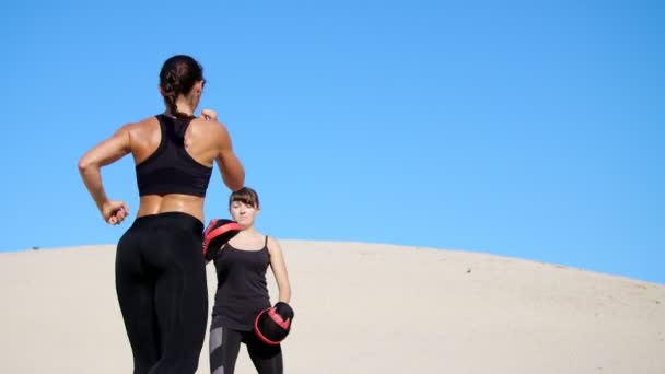 两个运动 年轻妇女在黑色的健身服从事一双 外出工作 培养继续战斗 空无一人的海滩 蓝色的天空 在夏天 炎热的太阳下 慢动作 — 图库视频影像