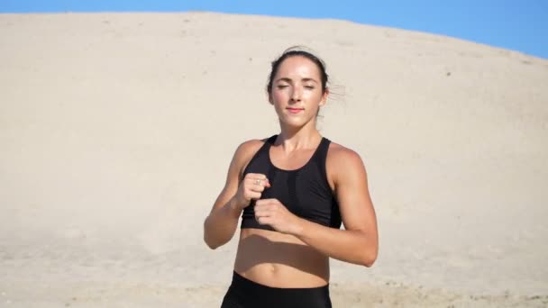 穿着黑色上衣的女运动员 运动员 练习踢腿 在镜头前踢脚 在一个荒芜的海滩上 在炎热的阳光下 慢动作 — 图库视频影像