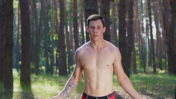 裸の胴 ジャンプロープを持つ若い運動選手は ゴムロープ クロスフィット要素との強度演習を実行します スローモーション 夏の松林の中で太陽の光の中で — ストック動画