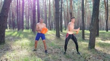 Bir çıplak, çıplak torsolar ile genç atletik erkek güç egzersizleri ağır plakalı crossfit gerçekleştirin. Ağır çekim. Çam ormanı içinde yaz, güneş ışınlarının
