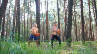 Bir çıplak, çıplak torsolar ile genç atletik erkek güç egzersizleri ağır plakalı crossfit gerçekleştirin. Ağır çekim. Çam ormanı içinde yaz, güneş ışınlarının