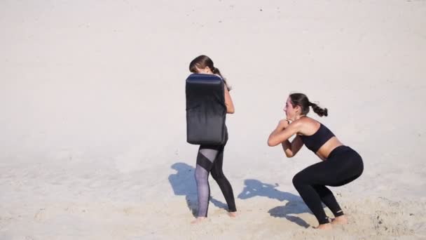 身着黑色健身两个运动 年轻妇女从事一双 外出工作 深蹲对执行和踢 Ups 荒芜的沙滩 在夏天 炎热的太阳下 — 图库视频影像