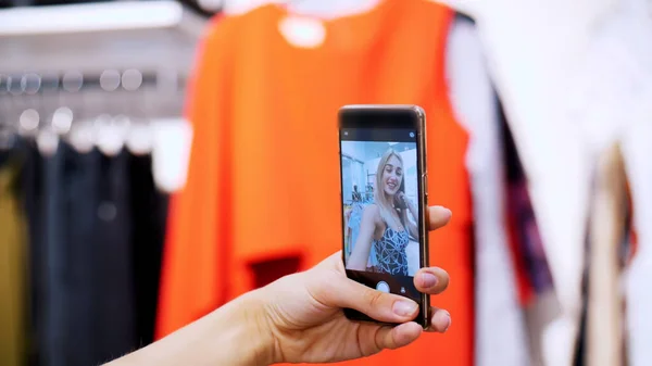 stock image Sexy girl, a beautiful blonde woman makes selfie in a new outfit, smiling, in a store, a boutique of clothes. In the frame is a female hand with a smartphone. slow motion. High quality photo