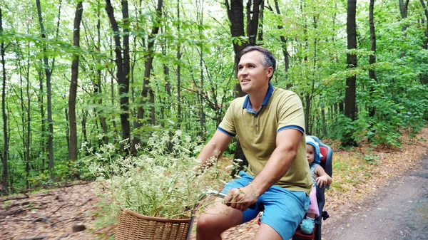 a man with a child riding a bicycle in the forest, in the summer, the child is sitting in a special chair. High quality photo
