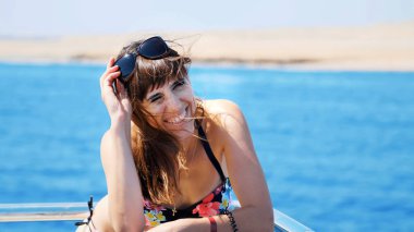 Yaz, deniz, portre, güzel esmer kadın mayo ve güneş gözlüğü takıyor, güvertede duruyor, dinleniyor, saçları rüzgarda dalgalanıyor, mutlu. Yüksek kalite fotoğraf