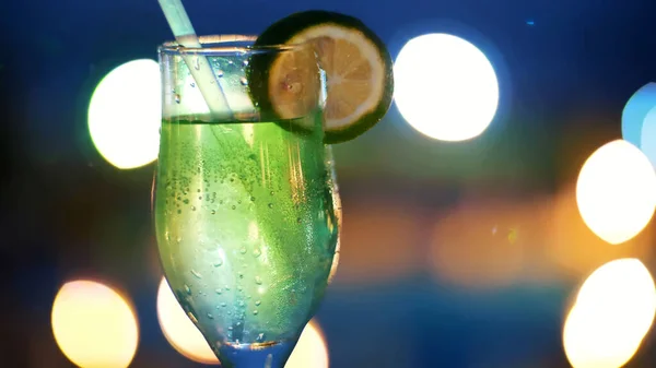 stock image cocktail party, drink with ice, in a glass with a straw and decorated with a slice of lemon, in the rays of soffits, lamps, flickering lights. original alcoholic and non-alcoholic cocktails. High