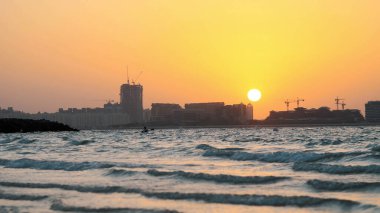 Dubai, BİRLİK ARAB EMIRATES, BAE - 20 Kasım 2017: Gün batımında, Sörf. Dalgalar kumda yuvarlanır ve üzerine yayılır. Şehir evlerinin ana hatları ışık huzmelerinde görülebilir. Yüksek kalite fotoğraf