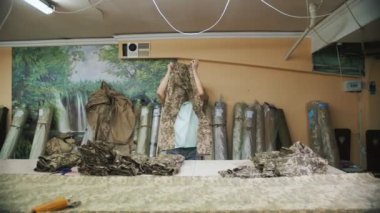 clothing quality check. a man checks the quality of sewing finished sewn clothing products and arranges them in piles by size. sewing of camouflage military clothes.