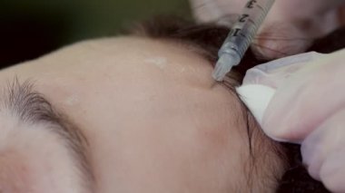 close-up. Doctor, in protective gloves, puts beauty injection to client forehead with syringe. Middle-aged woman gets beauty facial cosmetology procedure in healthcare clinic.