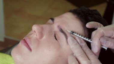 close-up. Doctor, in protective gloves, puts beauty injection to client forehead with syringe. Middle-aged woman gets beauty facial cosmetology procedure in healthcare clinic.