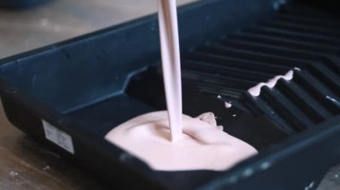Plastik tepside boya. Duvar resmi. Pembe boya siyah plastik tepsiye dökülüyor. Kapatın. Tamir işleri ve konut koşullarının iyileştirilmesi kavramı. Ağır çekim. Paten boyama. Yenileme tamamlandı