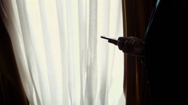 Akşam karanlığında, karanlıkta, pencerenin karşısında. Yakışıklı bir adam, beyaz gömlekli ve mavi ceketli bir işadamı akıllı bir telefon tutuyor, cep telefonuyla konuşuyor, evinde, yatak odasında. Yüksek kalite fotoğraf