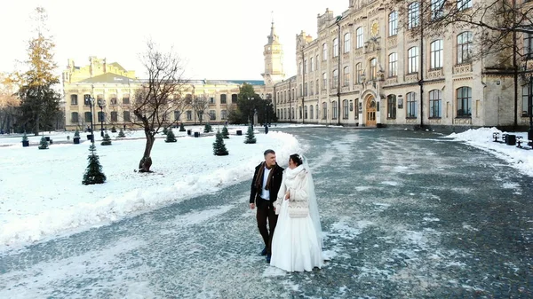 winter wedding. newlywed couple in wedding dresses are walking through the snow-covered park, against the background of ancient architecture and paving stones. High quality photo