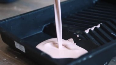 Plastik tepside boya. Duvar resmi. Pembe boya siyah plastik tepsiye dökülüyor. Kapatın. Tamir işleri ve konut koşullarının iyileştirilmesi kavramı. Ağır çekim. Paten boyama. Yenileme tamamlandı