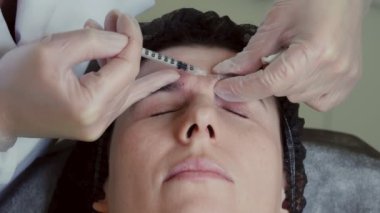 close-up. Doctor, in protective gloves, puts beauty injection to client forehead with syringe. Middle-aged woman gets beauty facial cosmetology procedure in healthcare clinic.