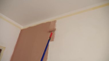 Duvar resmi. Su bazlı boya. Paten boyama. Onarım. Yakın plan. Boya silindiri kullanarak beyaz duvarı pembeye boyamak. Dairede, odada, evde, dairede tadilat yapıyor. Tamamlama ve inşaat işi