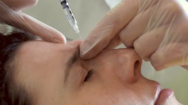 close-up. Doctor, in protective gloves, puts beauty injection to client forehead with syringe. Middle-aged woman gets beauty facial cosmetology procedure in healthcare clinic.